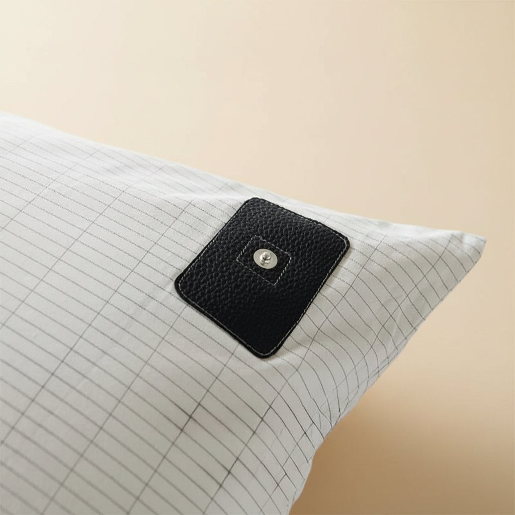 White pillow with a black square patch featuring a silver button on a white background